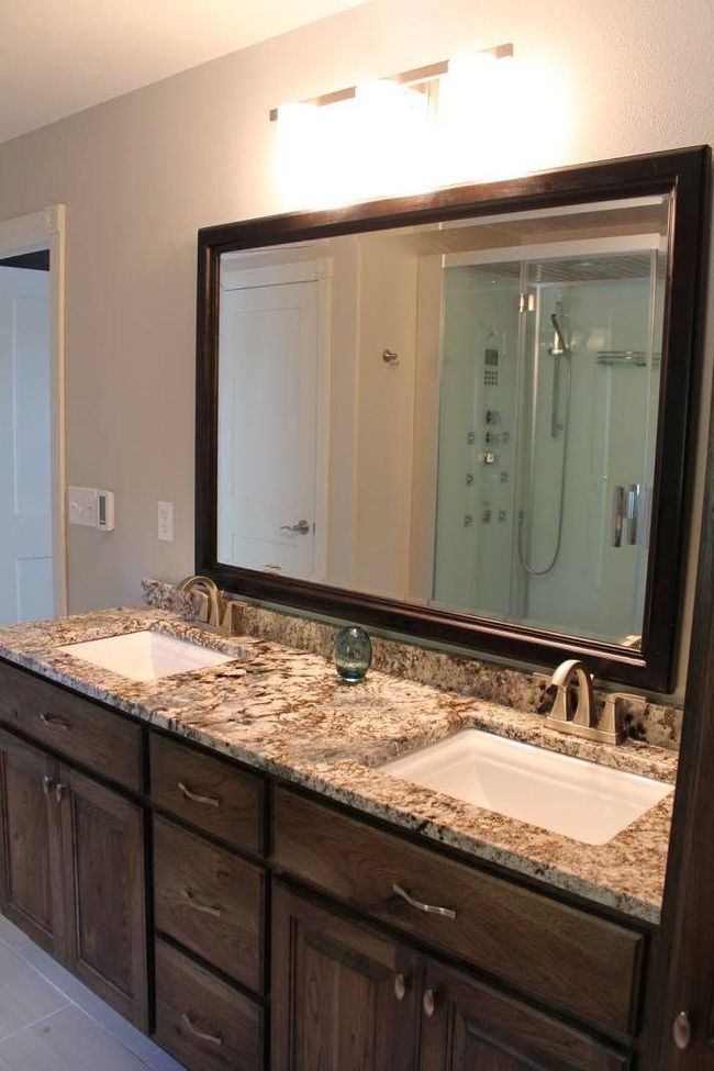 Bathroom vanity with double sinks, granite countertop, large mirror, and dark wood cabinets