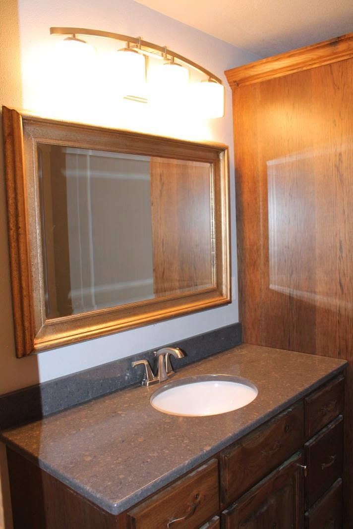 Bathroom vanity with dark wood cabinets, granite countertop, sink, and large mirror under a light fixture.