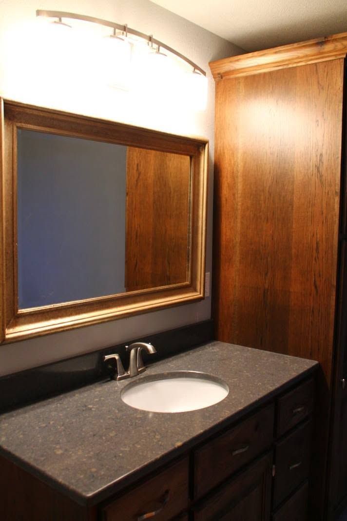 Bathroom vanity with dark countertop, round sink, large mirror, and wood cabinets