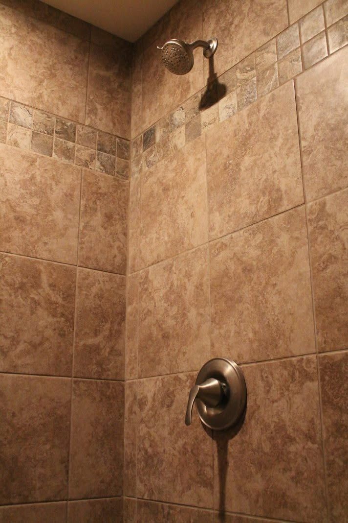 Shower stall with tan tile walls, a showerhead above, and a control handle below.