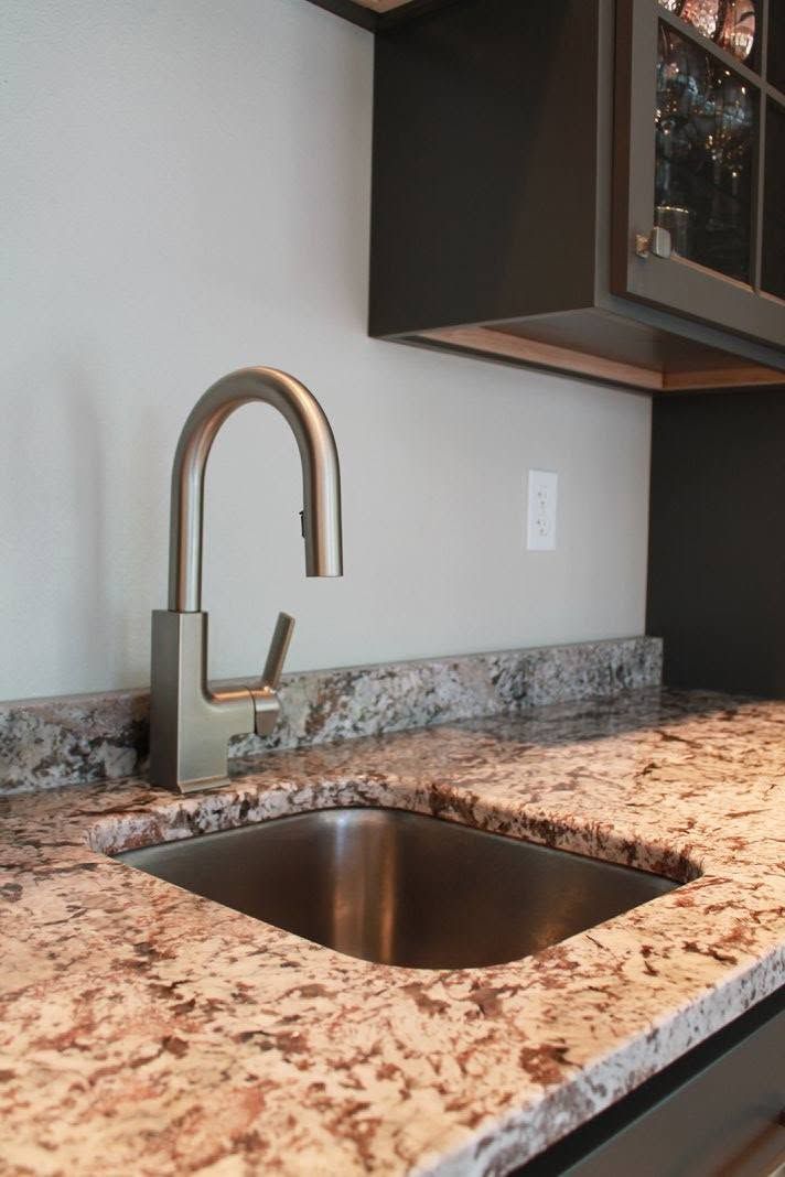 Kitchen sink with tall chrome faucet and speckled granite countertop beneath dark cabinets