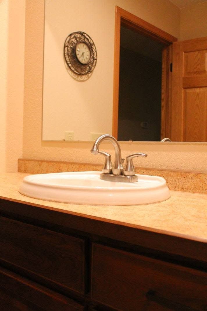 Bathroom sink with white basin and chrome faucet on a beige countertop, seen in a mirror.