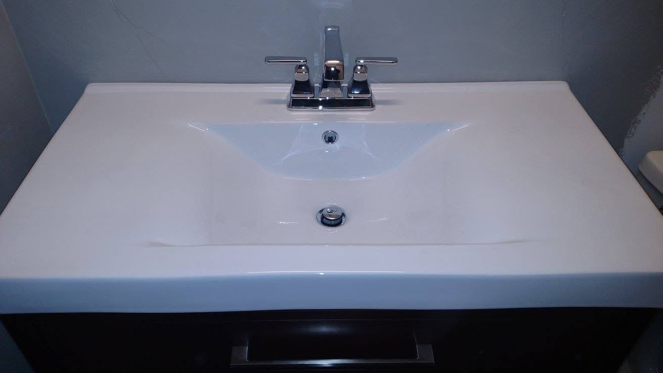 White bathroom sink with chrome faucet and drain against a gray wall, vanity below