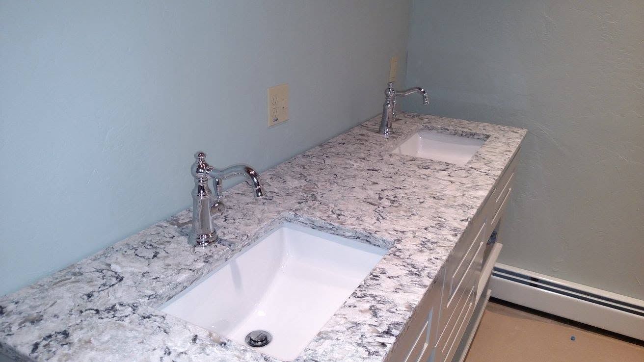 Empty restroom vanity with two sinks and speckled granite countertop against a light blue wall
