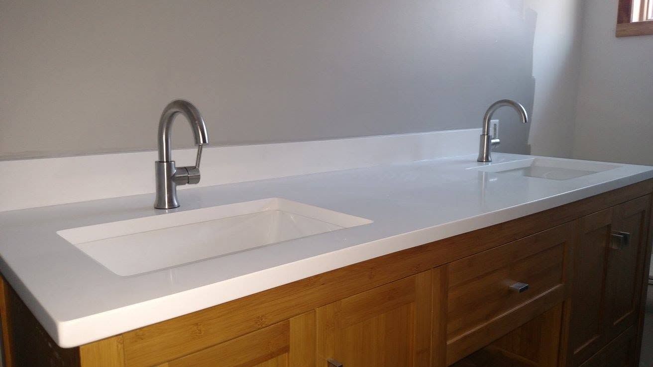 White bathroom countertop with two sinks and chrome faucets above wood cabinets