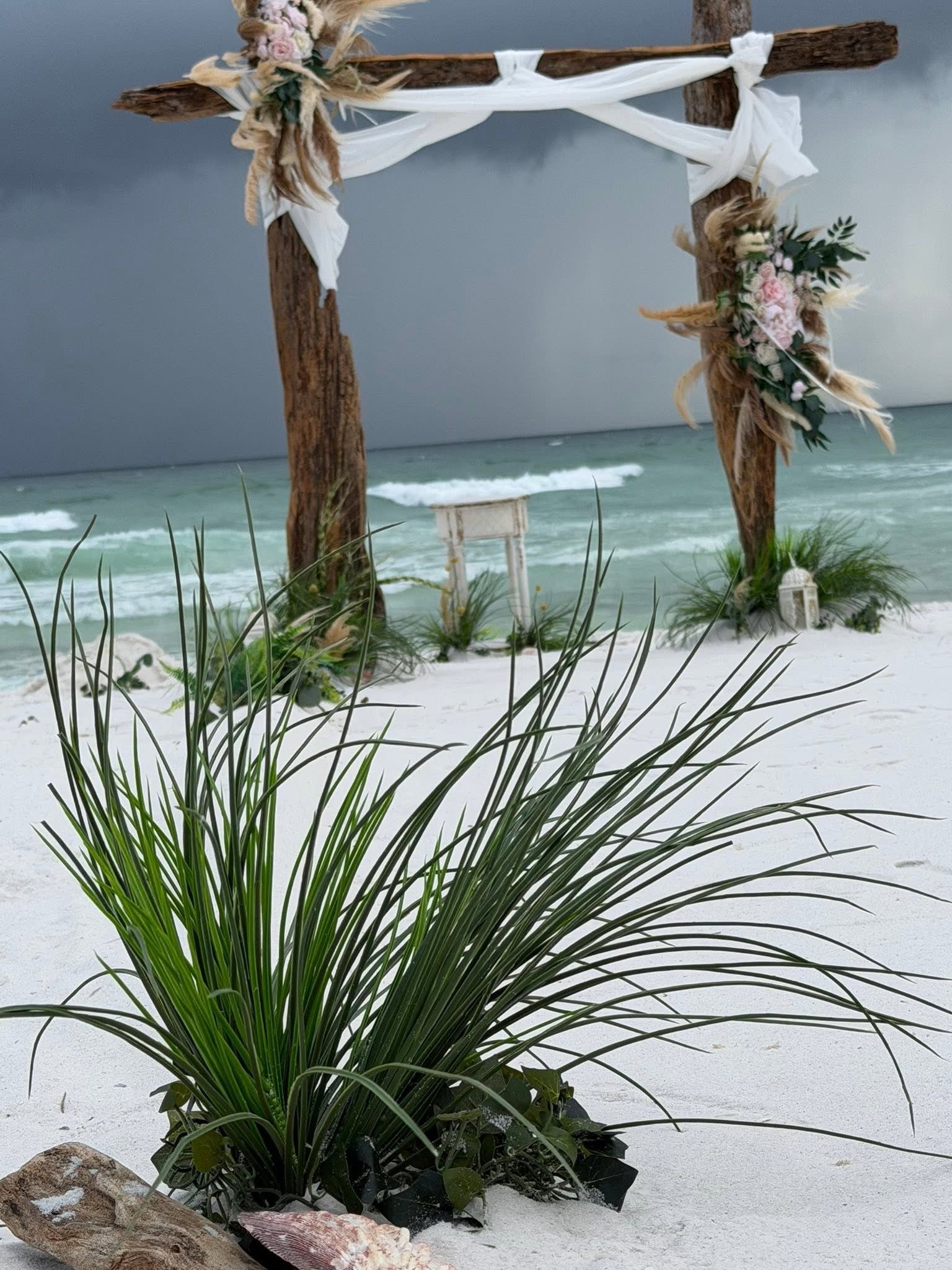 Beach wedding arch on a windy shoreline with ocean waves and white floral decorations