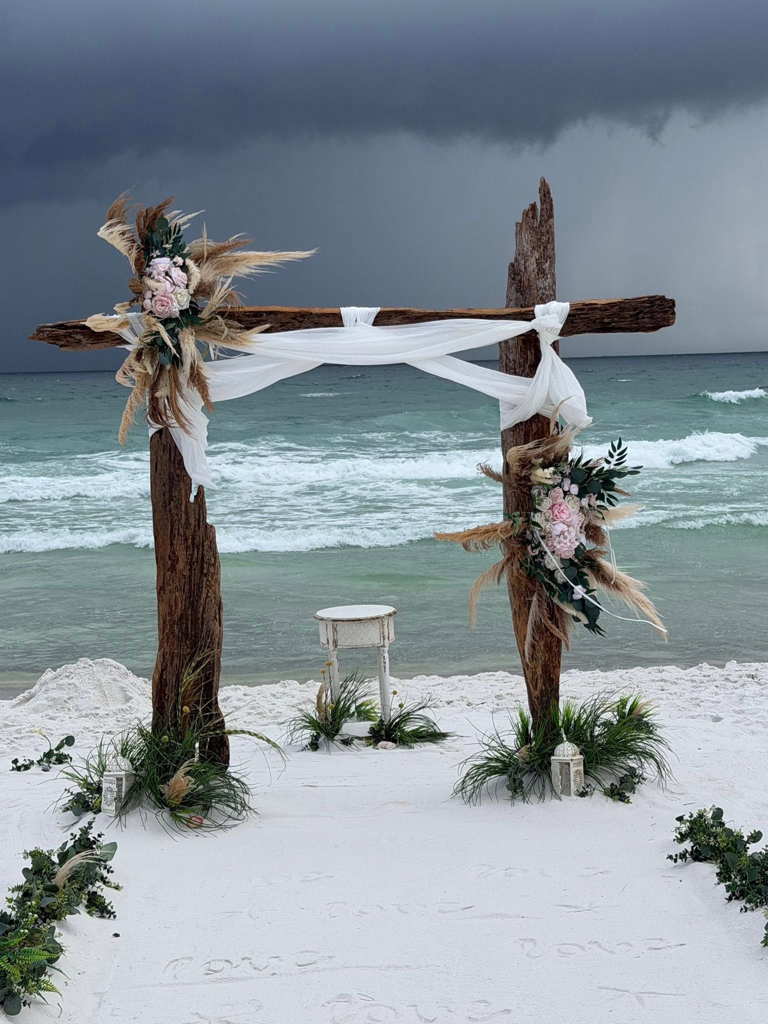 Snowy beach arch with floral decorations facing rough ocean under dark storm clouds.