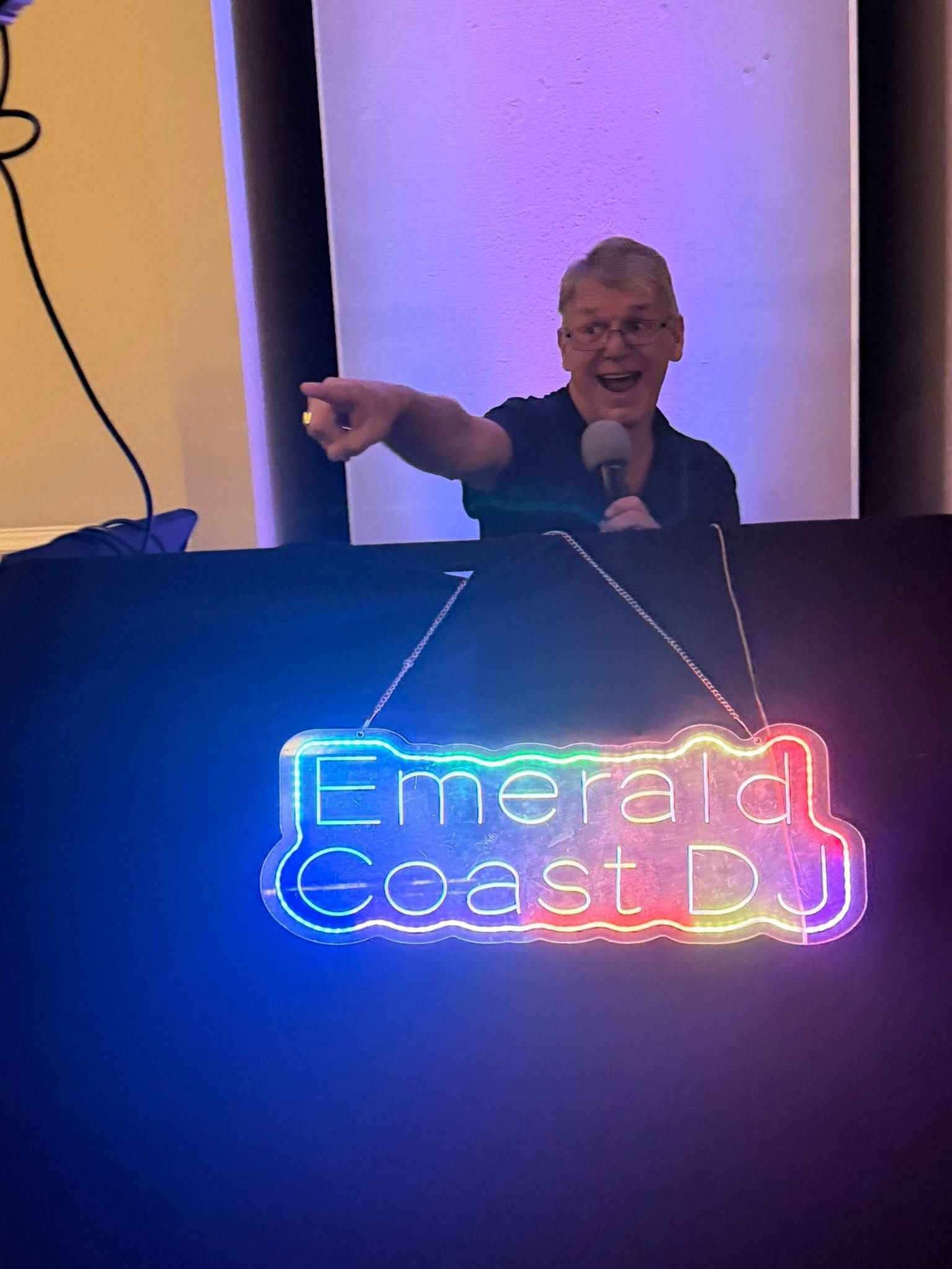 Person speaking at a podium with a glowing neon “Emerald Coast” sign in front of them