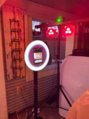 Ring light and photo booth setup in a dim room with red lights and a camera stand.