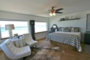 Bright bedroom with large windows, king bed, gray chairs, lamp, and patterned bedding.