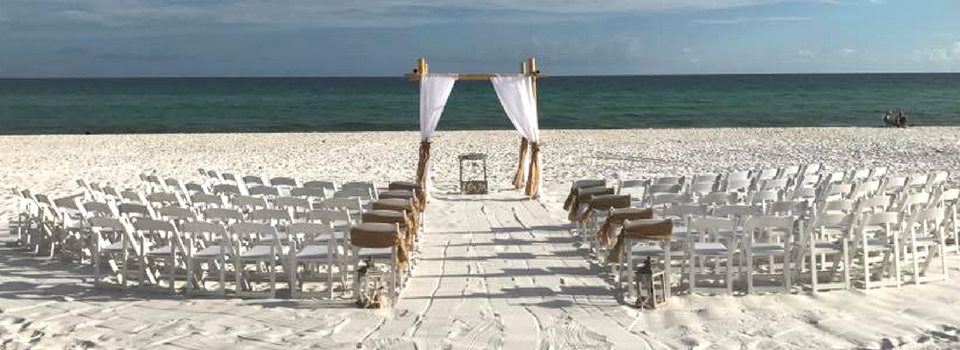 White chairs and a wedding arch on a sandy beach facing the ocean under a cloudy sky