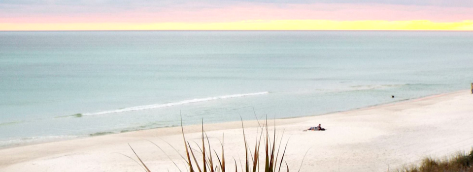 Calm beach shoreline at sunrise with pale pink sky and gentle waves