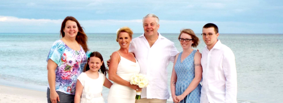 Five people posing together on a beach, with ocean waves in the background.