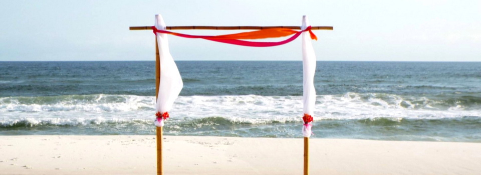 White beach wedding arch with red drapes facing the ocean on a sandy shore