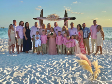 Wedding party posing on a sunny beach under a wooden arch with pampas grass.
