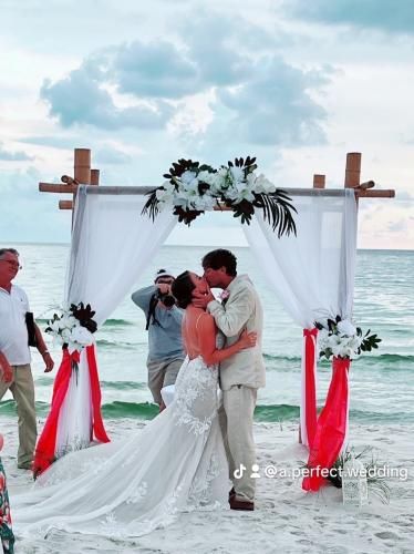 Beach wedding couple embracing under a floral arch beside the ocean at sunset