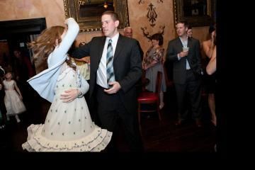 Bride and groom dancing at a formal indoor reception, with guests watching nearby.