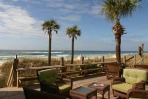 Beachfront patio with wicker chairs and tables overlooking the ocean, lined by palm trees