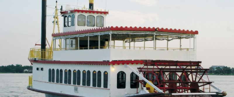 White two-deck riverboat with red trim on calm water, side view.