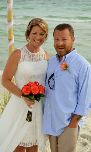 Bride and groom standing on a beach, smiling, with ocean waves behind them