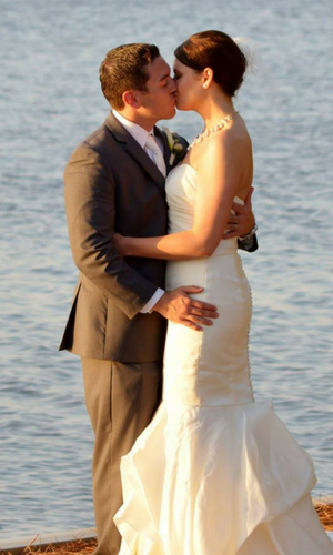 Couple kissing on a beach at sunset, the bride in a white dress and the groom in a gray suit