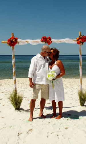 Couple kissing under a flower-decorated beach arch beside the ocean