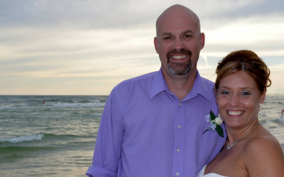 Smiling couple in dress clothes posing on a beach with ocean waves behind them