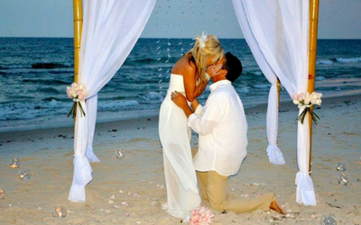 Couple kissing on a beach under a white canopy, with ocean waves in the background