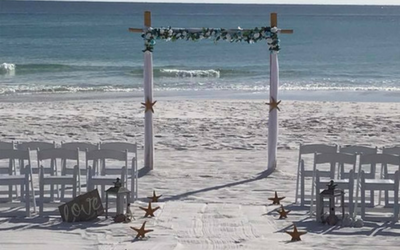 Beach wedding arch facing the ocean, flanked by white chairs on the sand with starfish decor.