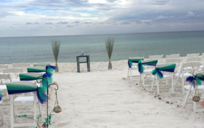 White beach aisle with turquoise chairs facing the ocean, decorated for a seaside ceremony