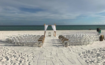 White wedding chairs arranged on a beach aisle facing a small altar by the ocean.