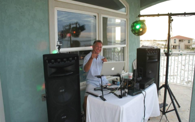 DJ performing beside speakers and a laptop on a patio deck