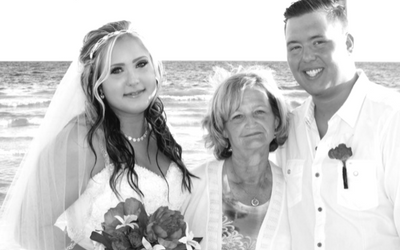 Bride and groom posing with an older woman on a beach, all smiling in wedding attire