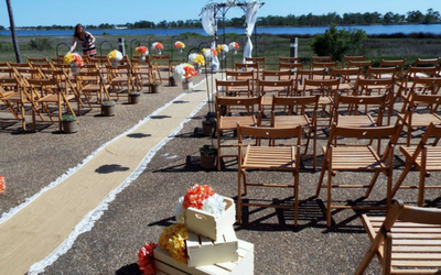 Outdoor wedding ceremony setup with wooden chairs and a flower-lined aisle by the water