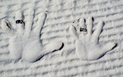 Two handprints pressed in white sand, with rings on two fingers and small objects in the palms.