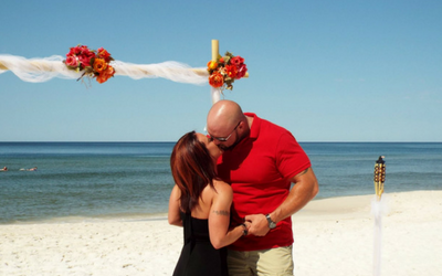 Couple in red holding each other on a beach wedding setup by the sea