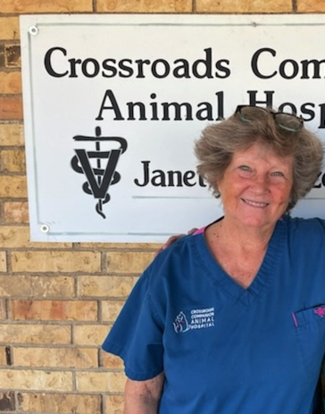 Woman in blue scrubs smiling beside a Crossroads Animal Hospital sign.
