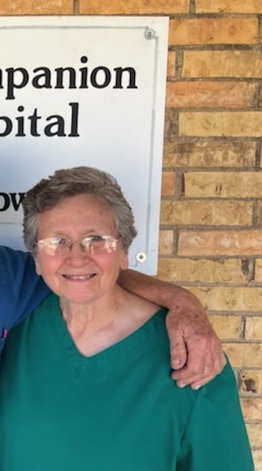 Smiling woman in a green top standing by a hospital sign and brick wall