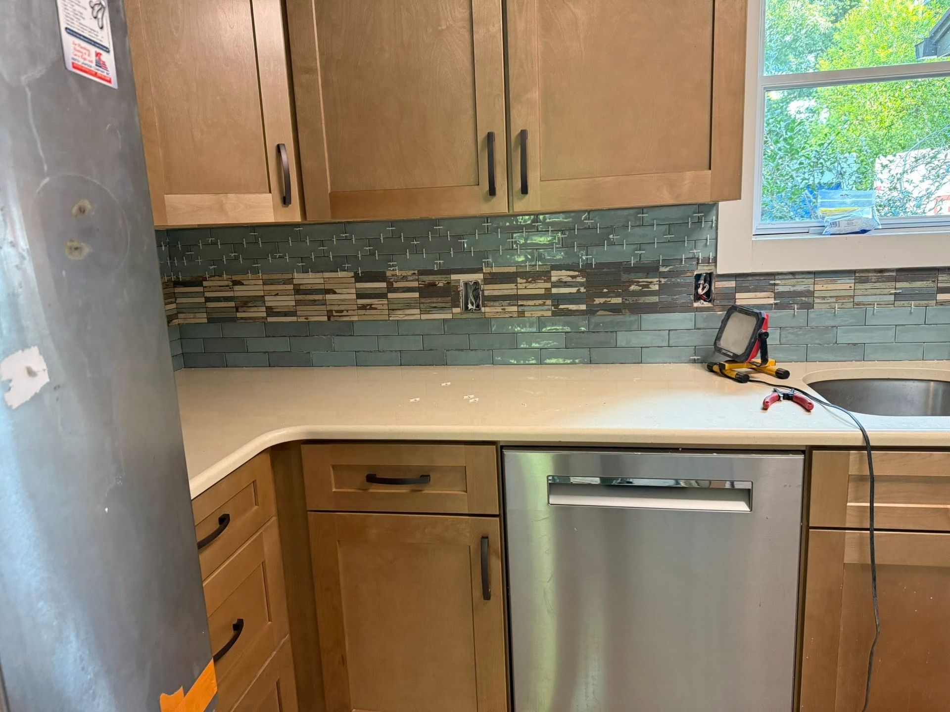 Small kitchen with wood cabinets, stainless dishwasher, gray fridge edge, and a window over the counter.