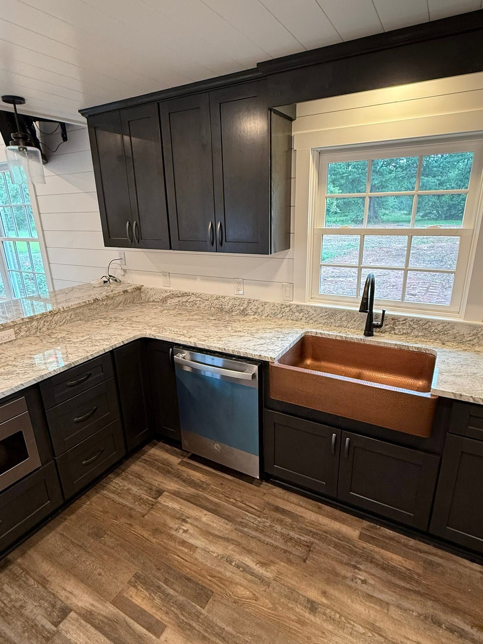 Modern kitchen with dark cabinets, granite counters, blue dishwasher, farmhouse sink, and wood floors.