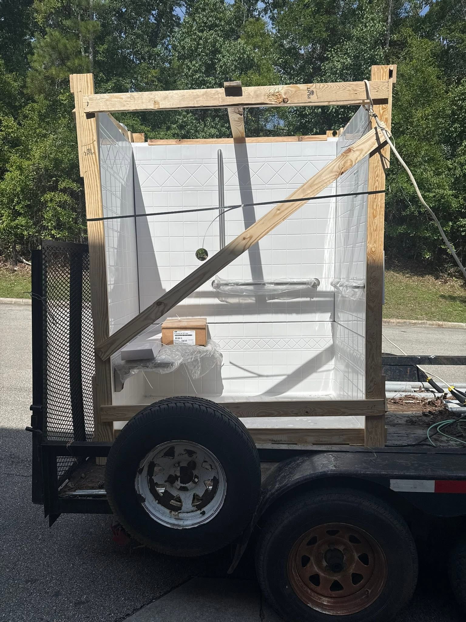 White appliance strapped to a trailer with wooden braces and a diagonal support bar outdoors