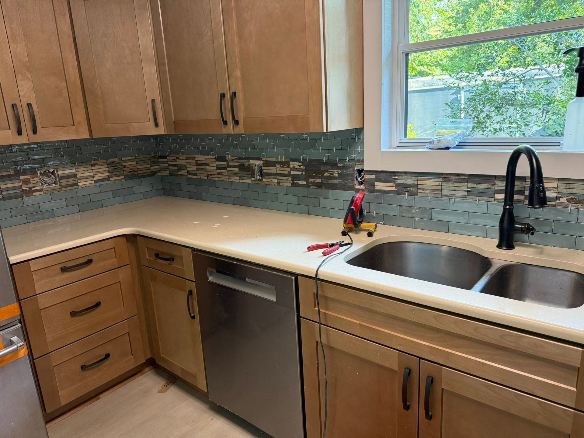 Small kitchen with wood cabinets, white counters, double sink, dishwasher, and window above the sink.