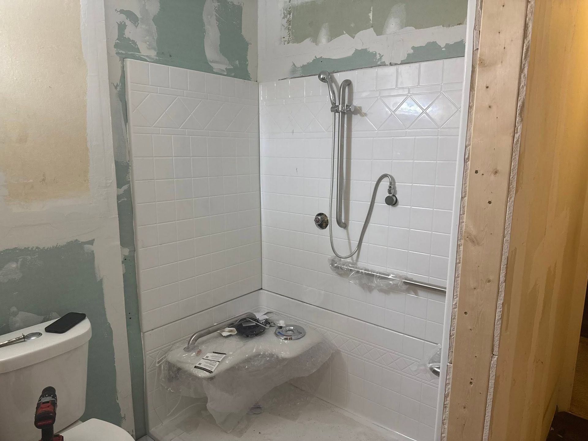 Small bathroom with a shower, toilet, and sink, showing partially tiled walls and renovation in progress