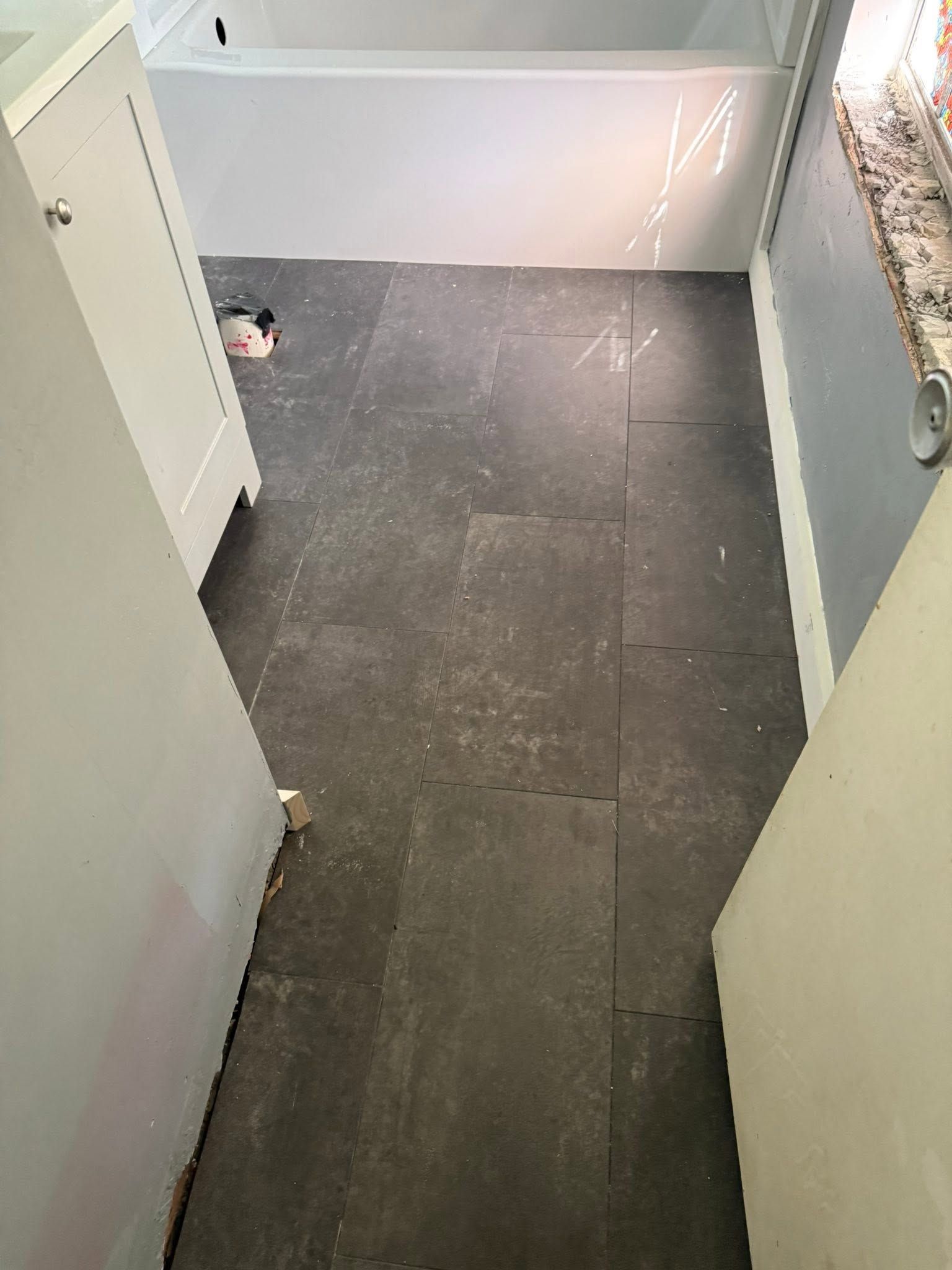 Narrow hallway with dark tile floor leading to a white bathtub or shower area.