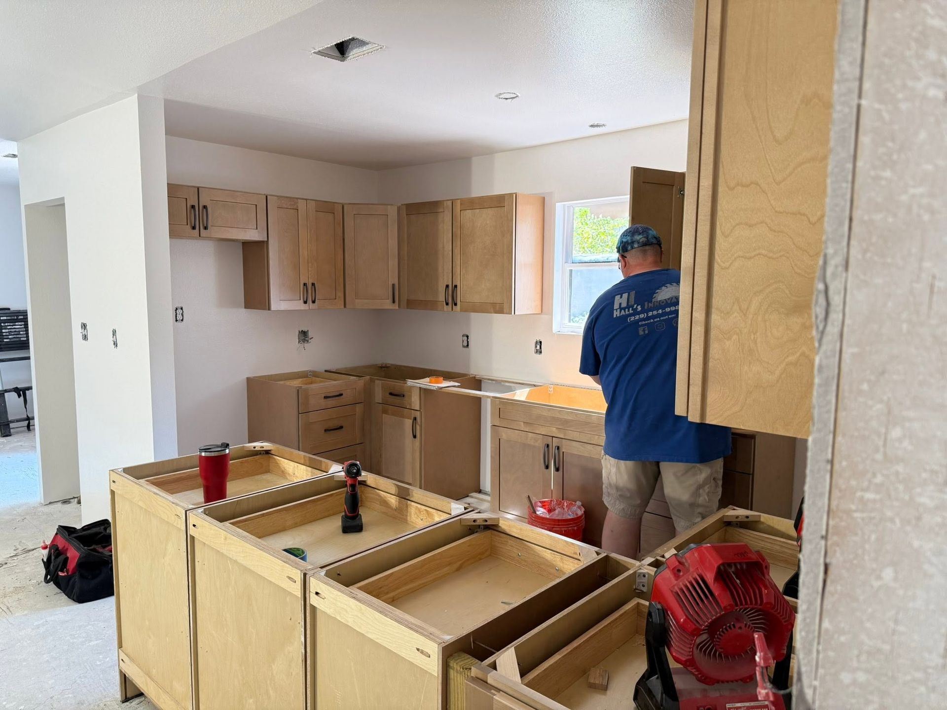 Kitchen remodel in progress with unfinished cabinets and a worker installing cabinetry.