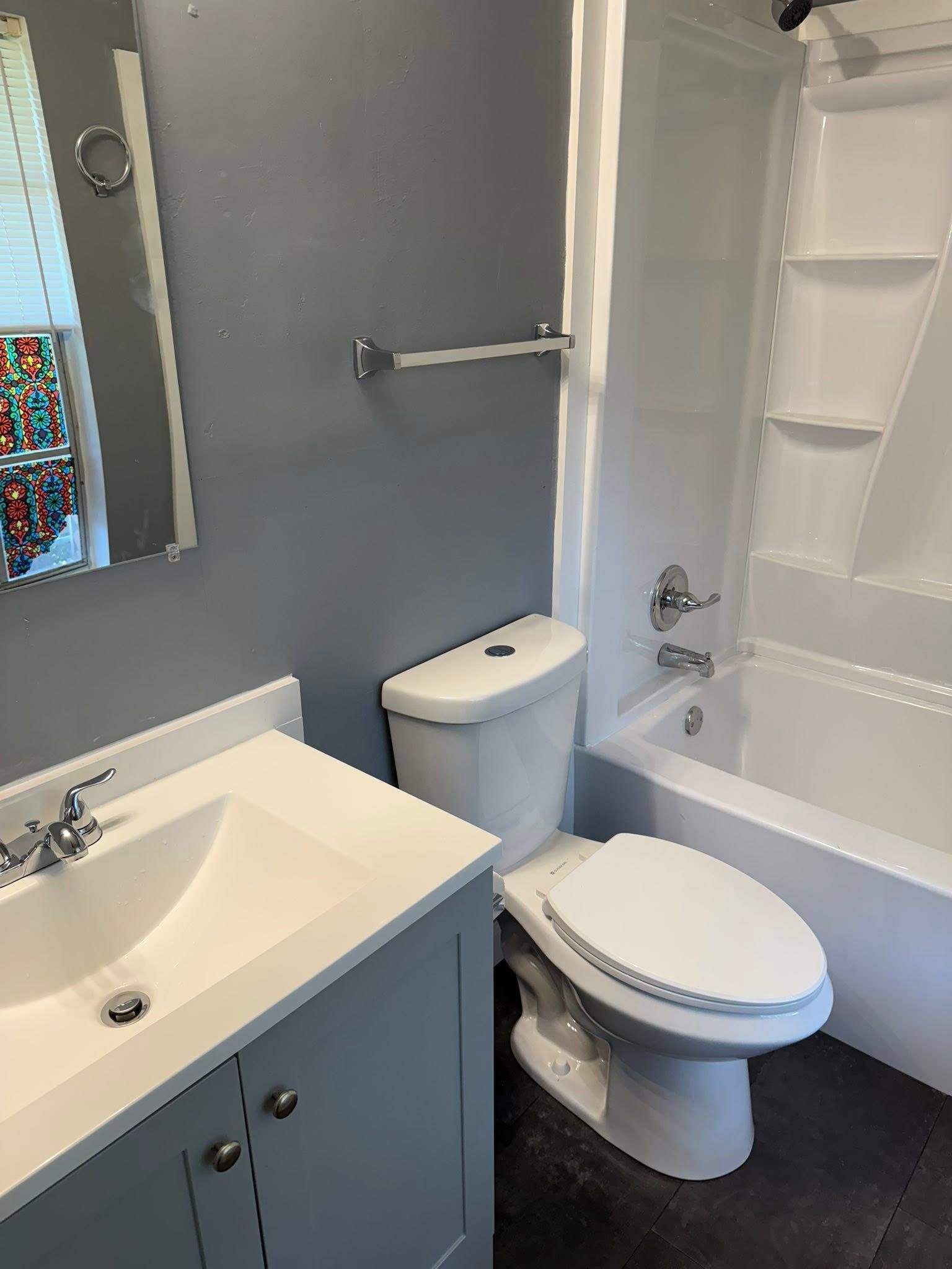 Small bathroom with blue vanity, white toilet, tub-shower, and gray walls