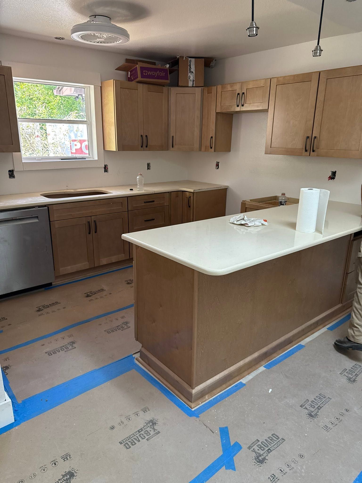 Unfinished kitchen with wood cabinets, island, sink window, and blue tape marking the floor.