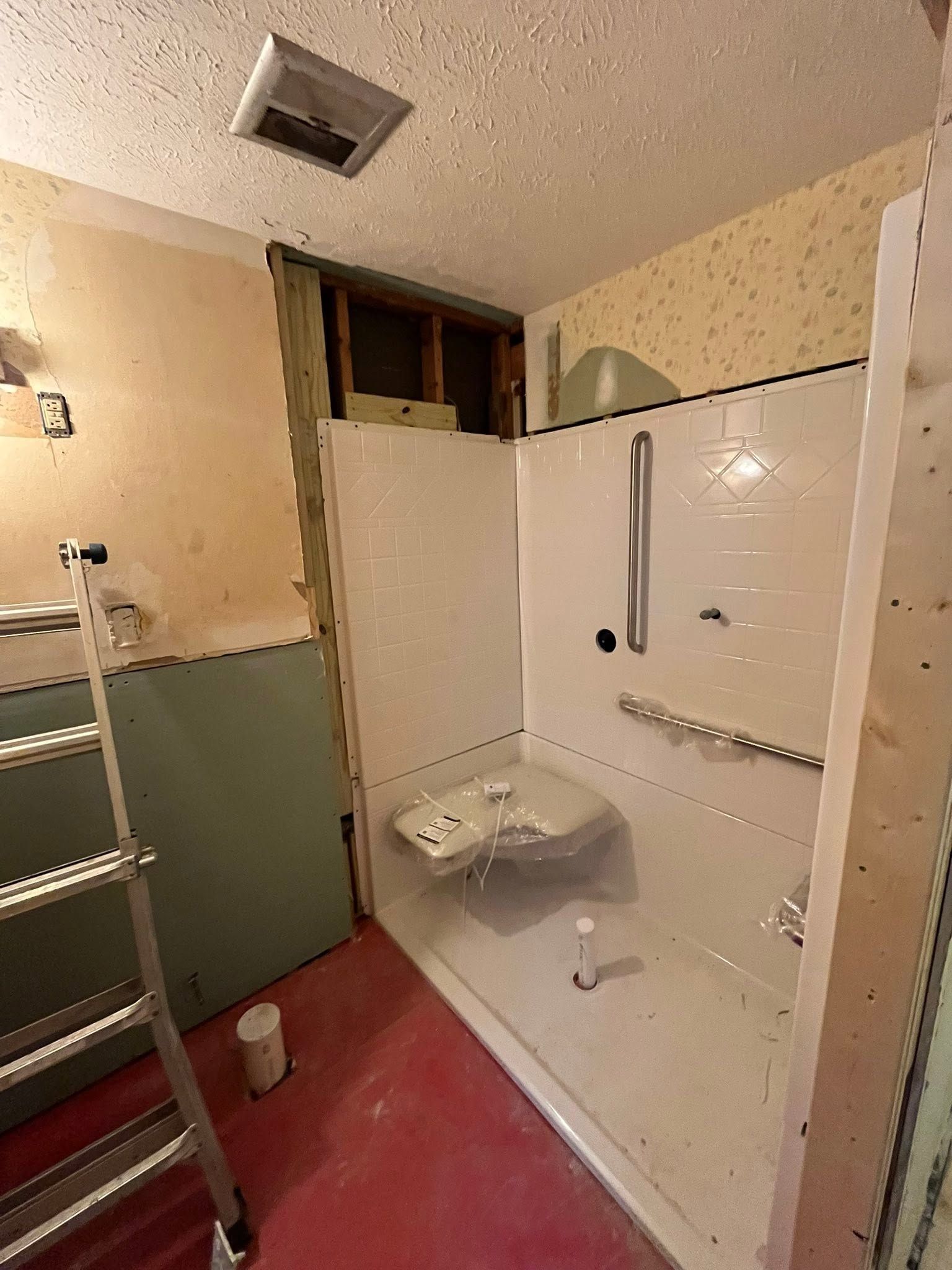 Small bathroom under renovation with shower, toilet, ladder, and exposed wall framing.