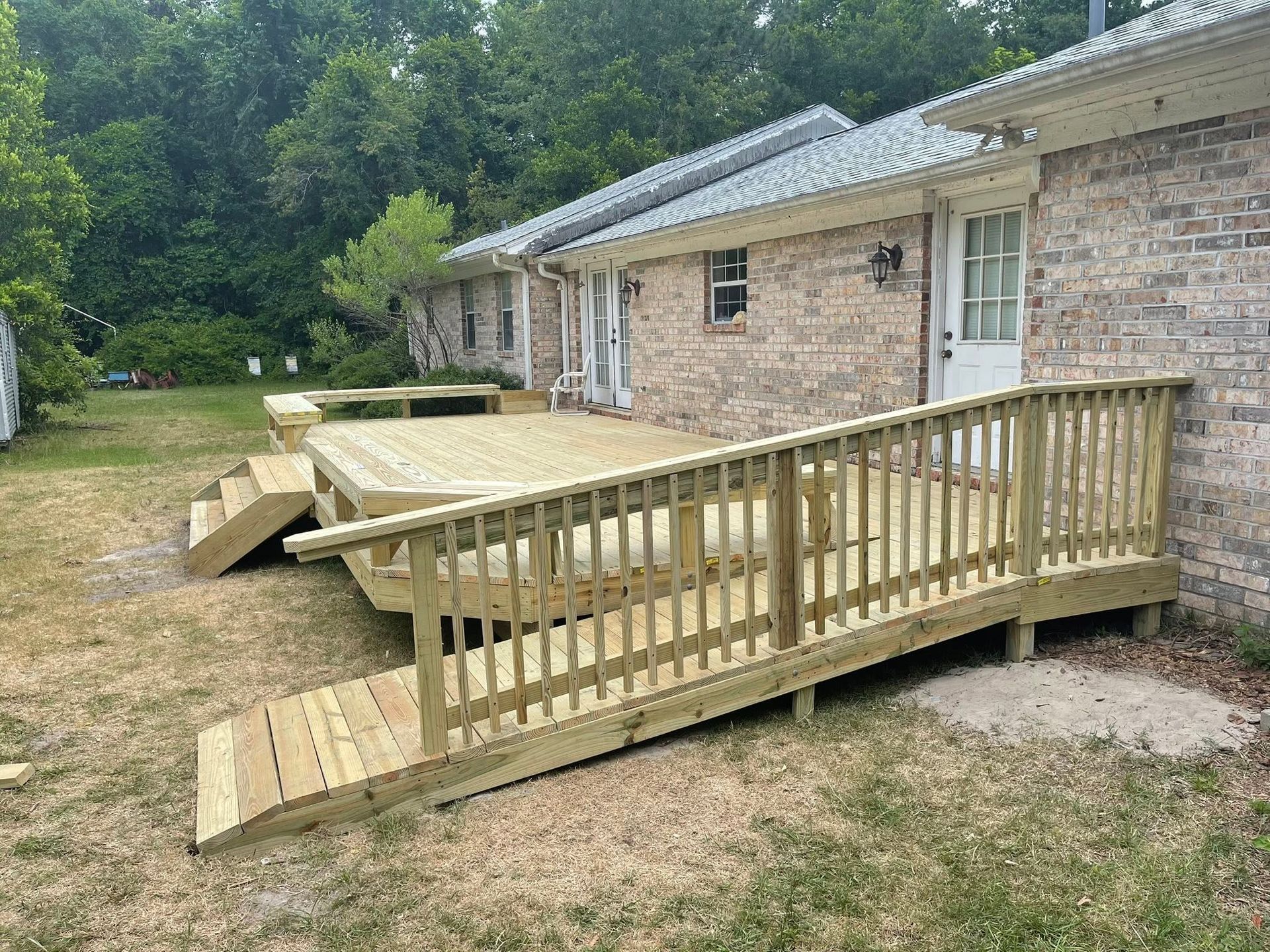 Wooden accessibility ramp and deck beside a brick house with a small porch