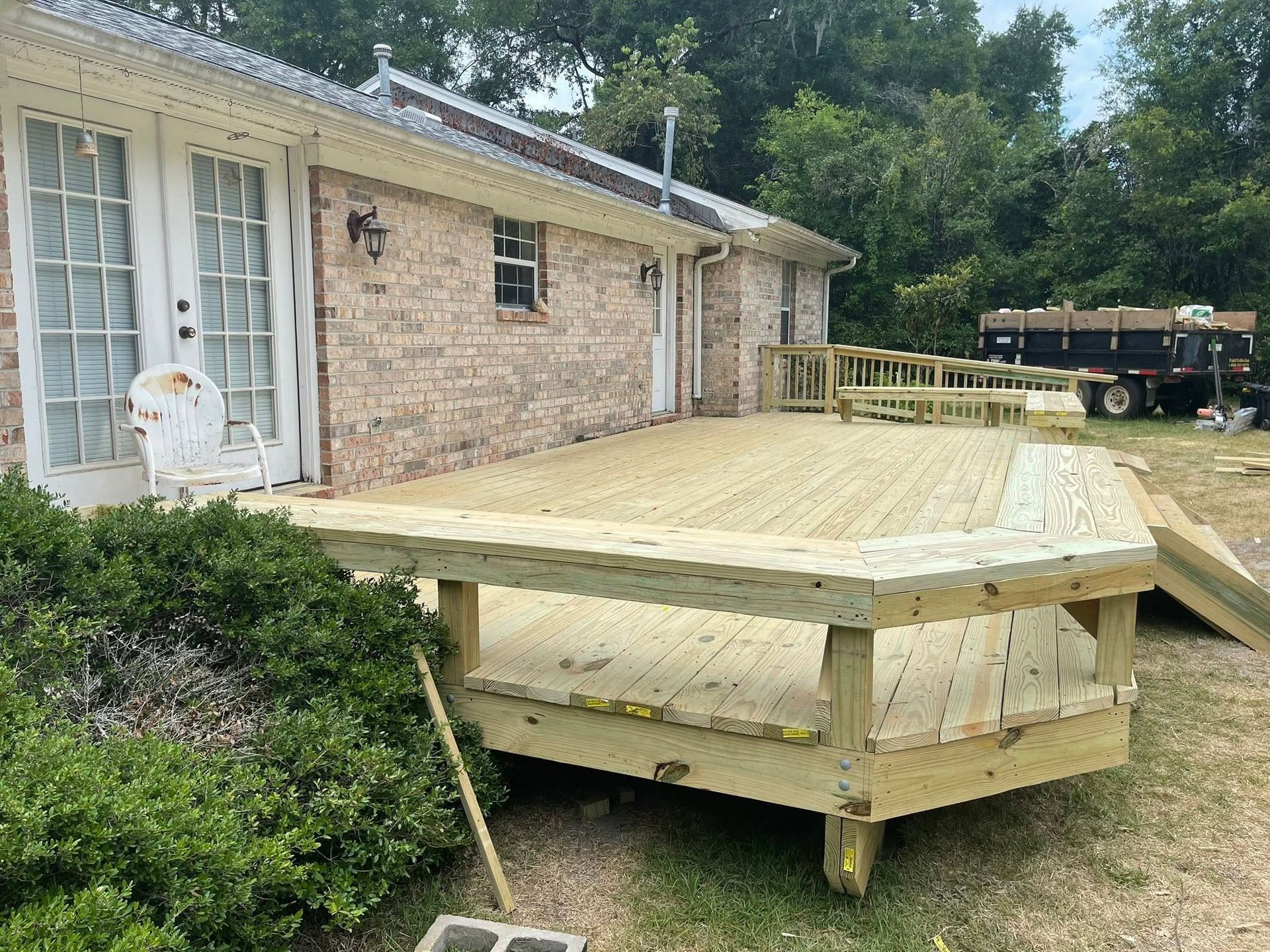 Wooden deck under construction beside a brick house, with a ramp in the foreground.